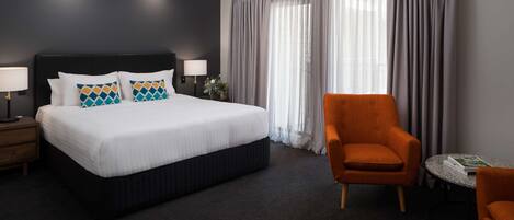 Une chambre d’hôtel avec un grand lit, une table de chevet avec une lampe, une chaise et une petite table avec un livre.