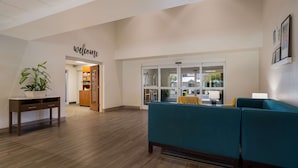 A lobby with a 'welcome' sign, a reception desk, a blue sofa, and a potted plant. - MainStay Suites Wilmington - University Area (Wilmington)