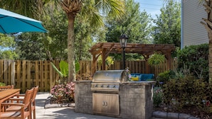 An outdoor kitchen with a grill, a wooden table with chairs, and a pergola with a hanging light. - MainStay Suites Wilmington - University Area (Wilmington)