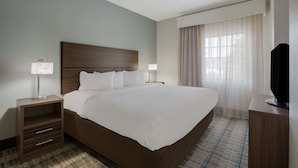 A hotel room with a large bed, two bedside tables, a TV, and a window with curtains. - MainStay Suites Wilmington - University Area (Wilmington)