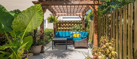 A covered patio area with a wooden pergola, a blue sofa, and a small table.