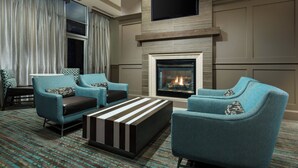 A modern living room with two teal armchairs, a black and white striped ottoman, a fireplace, and a flat-screen TV mounted above the mantel. - Residence Inn by Marriott Houston Downtown/Convention Center (Houston)