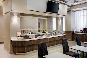 A hotel breakfast area with a buffet counter, seating, and a television above.