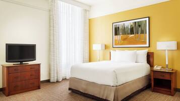 A hotel room with a bed, a television on a wooden dresser, two bedside lamps, and a painting on the wall.