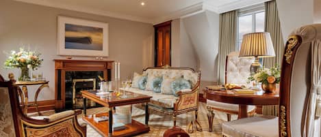Una habitación con sofá, sillones, una mesa, chimenea y un cuadro en la pared.