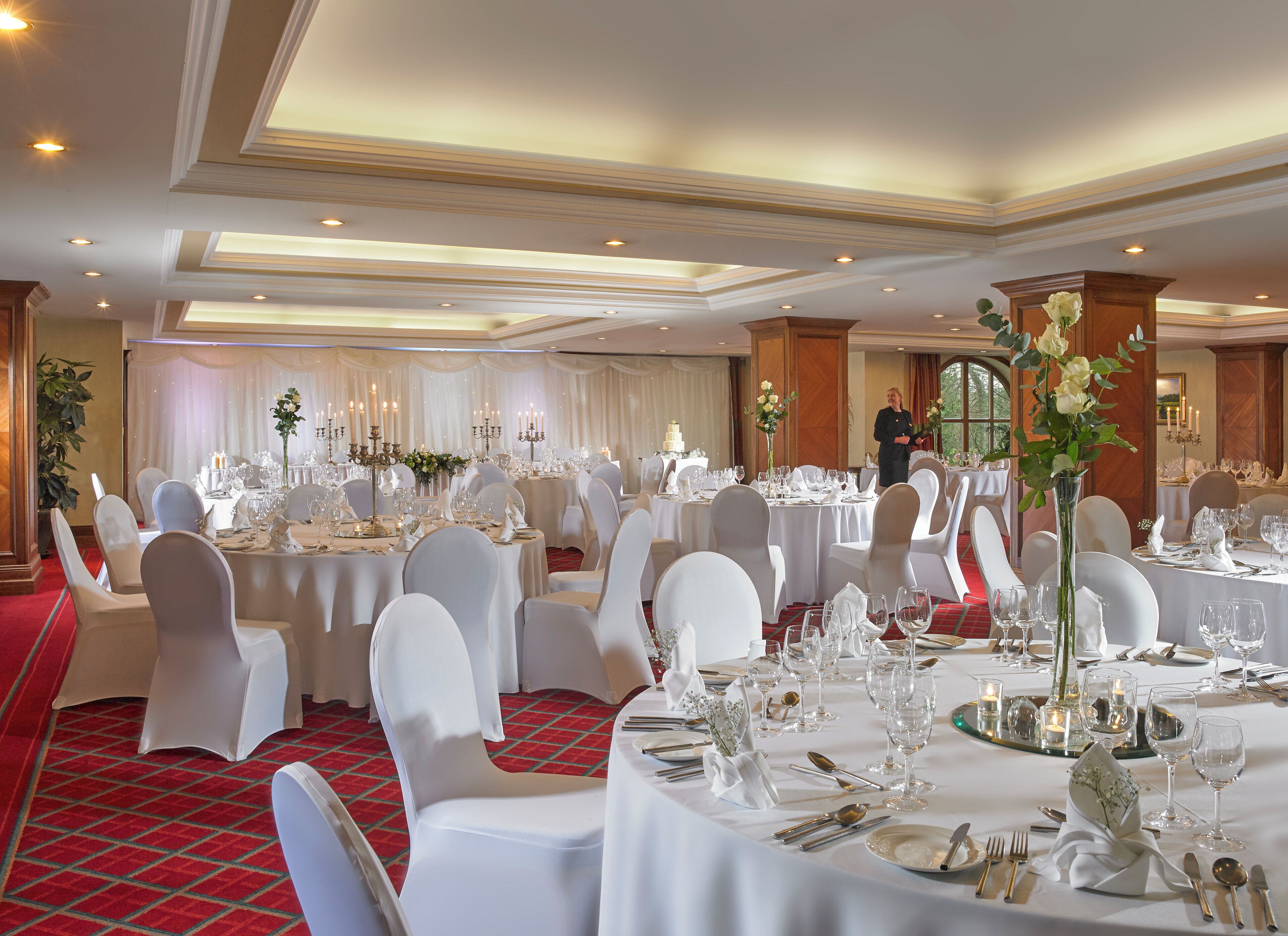 Une salle de banquet avec des tables rondes, des chaises blanches et des lustres.