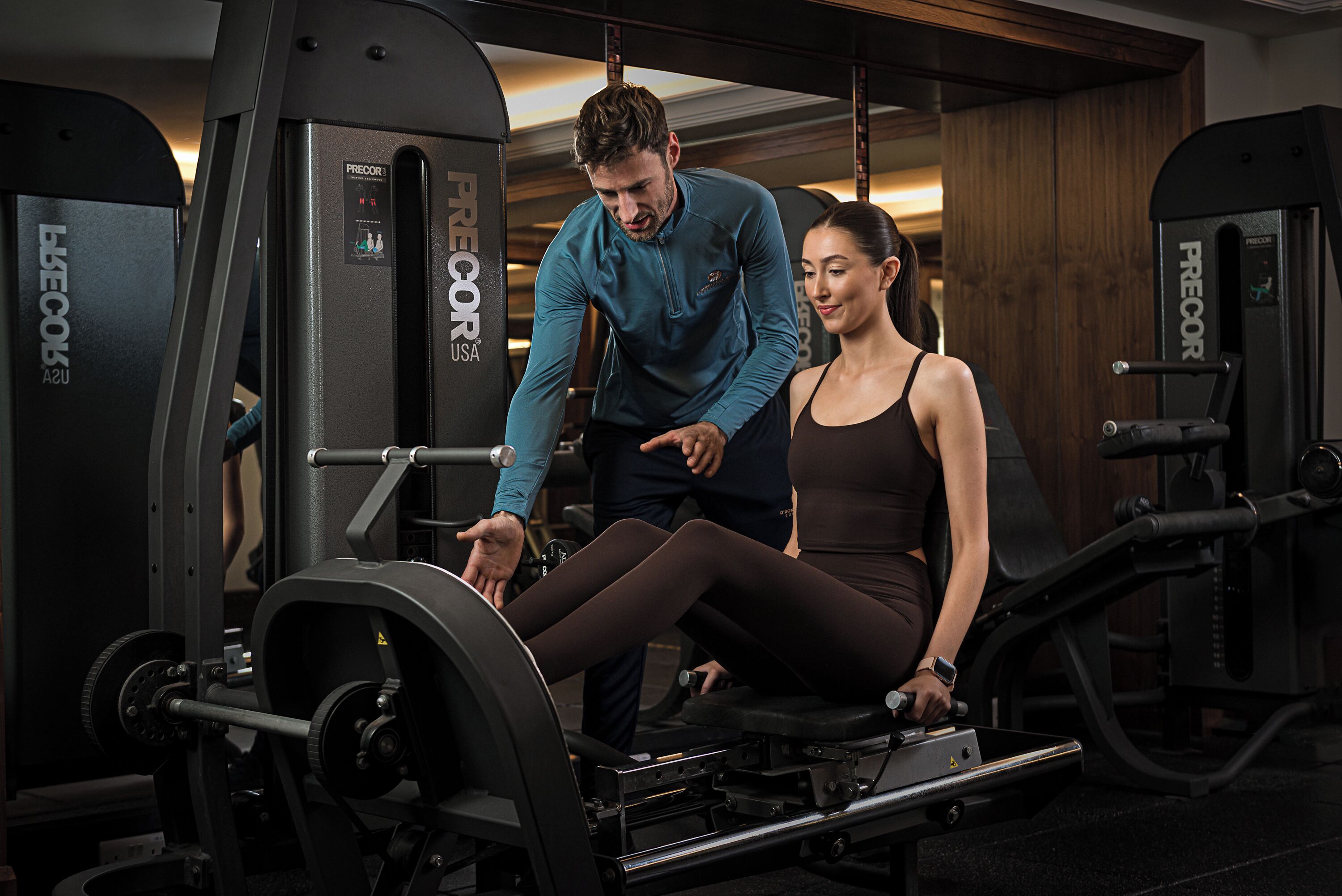 A gym with weight machines, a seated leg press, and a person using the equipment.