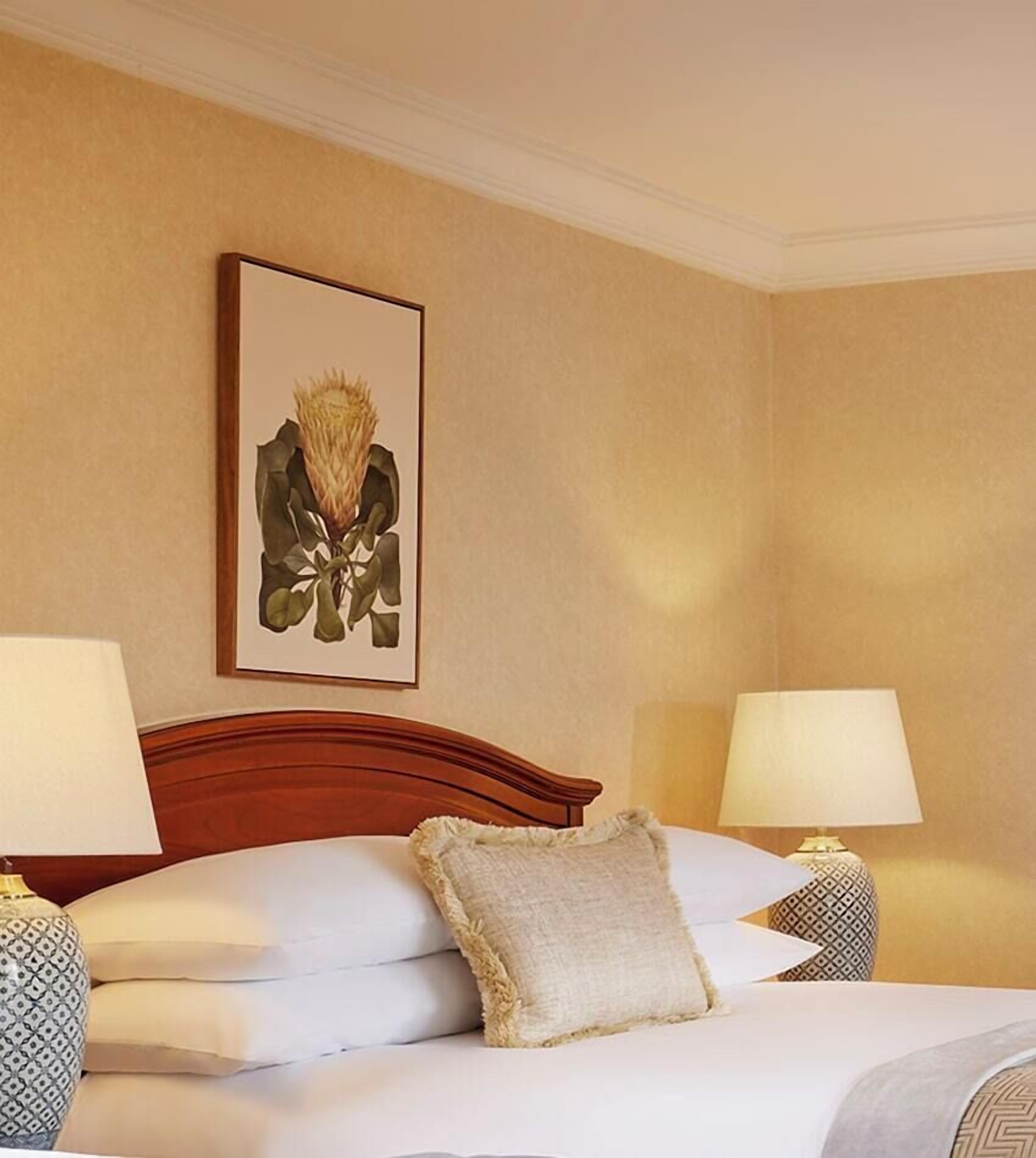 Une chambre d’hôtel avec un lit, deux lampes de chevet, une œuvre d’art encadrée au mur et une table de chevet à motifs.
