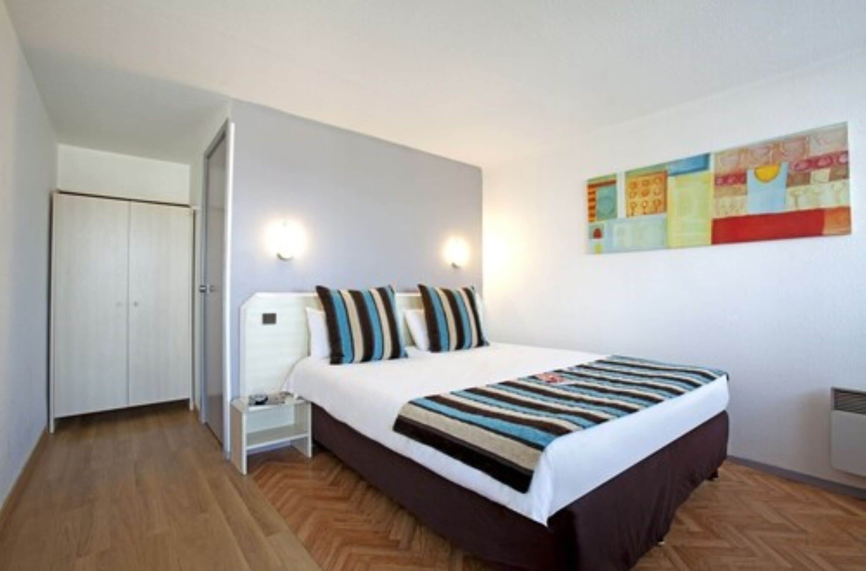 Une chambre à coucher comprenant un lit, des tables de chevet, une armoire et une œuvre d’art accrochée au mur.