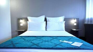Une chambre d’hôtel avec un grand lit, deux tables de chevet avec des lampes, une couvre-lit à motifs bleus et une fenêtre avec des rideaux.