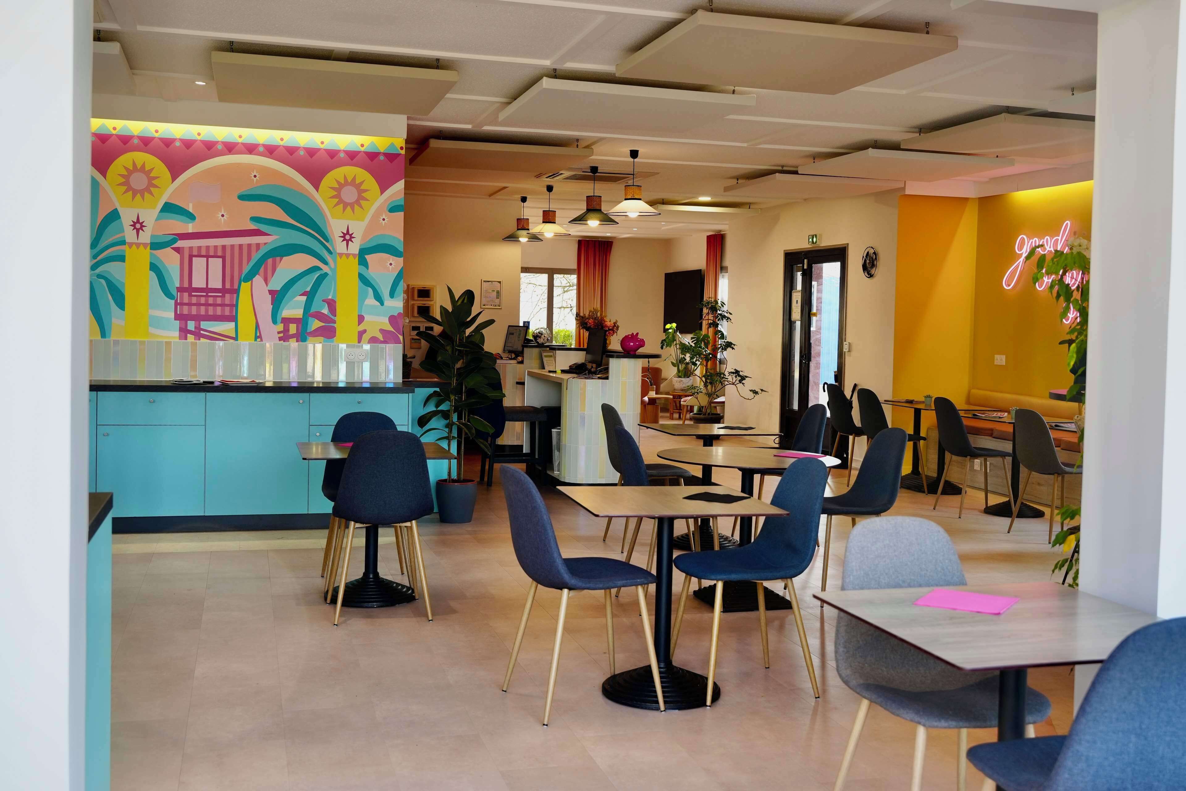 Una cafetería moderna con decoración azul y amarilla, que incluye mesas, sillas, una barra y un mural en la pared.