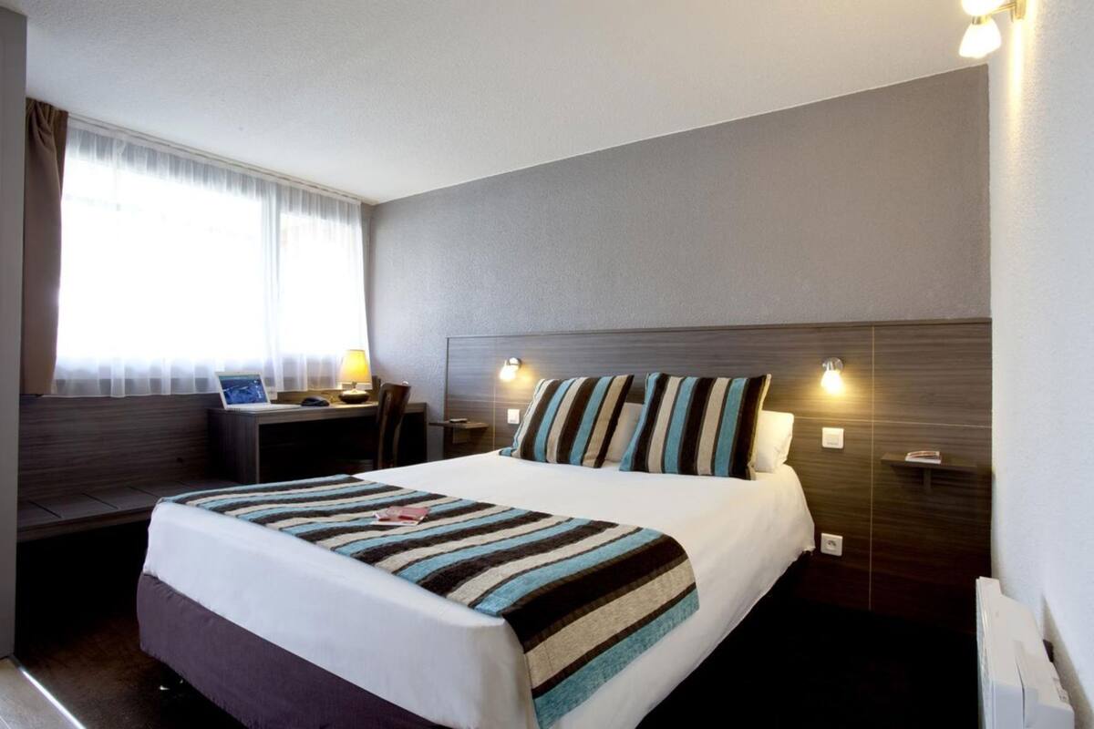 A hotel room with a bed, a desk, and a chair.