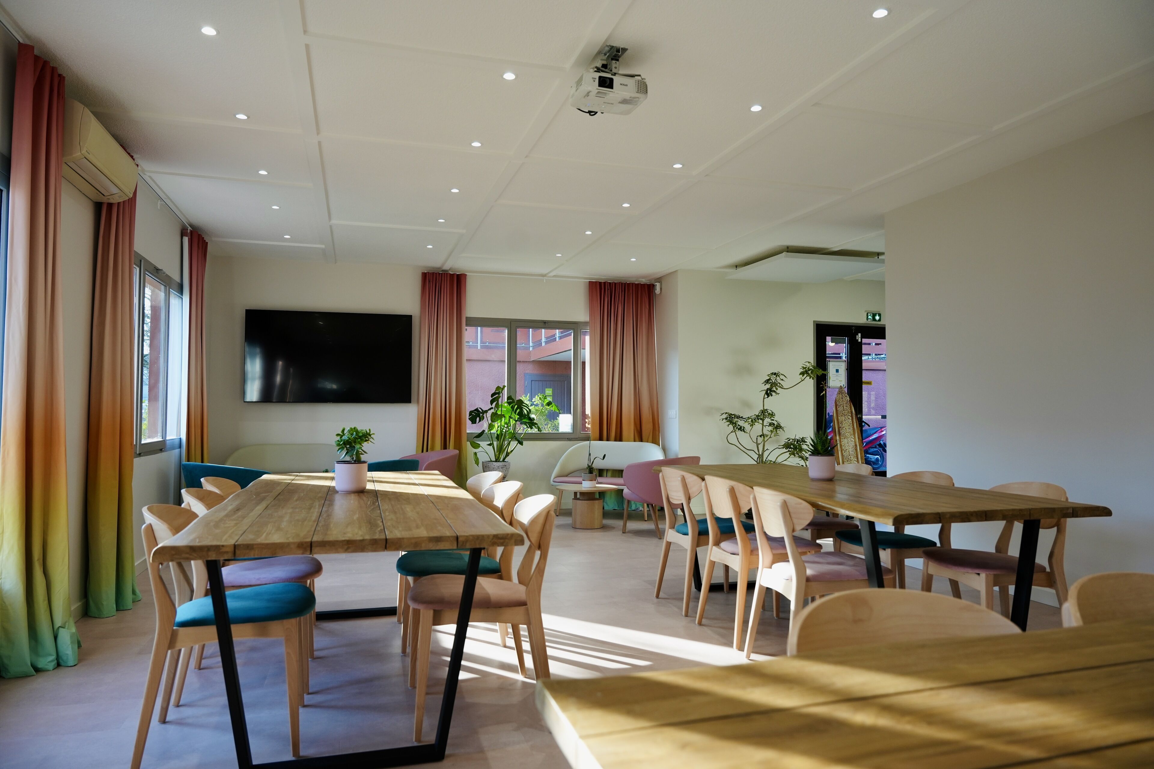 A conference room with a large table, multiple chairs, a flat-screen TV, and potted plants.