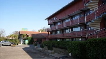 Ein Hotel mit roter Fassade, mehreren Balkonen und einem Parkplatz mit einem Auto.