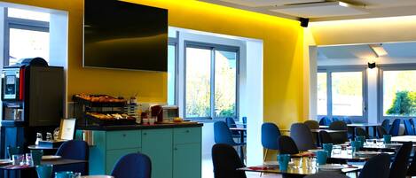 A modern dining area with yellow walls, blue chairs, and a large TV screen.