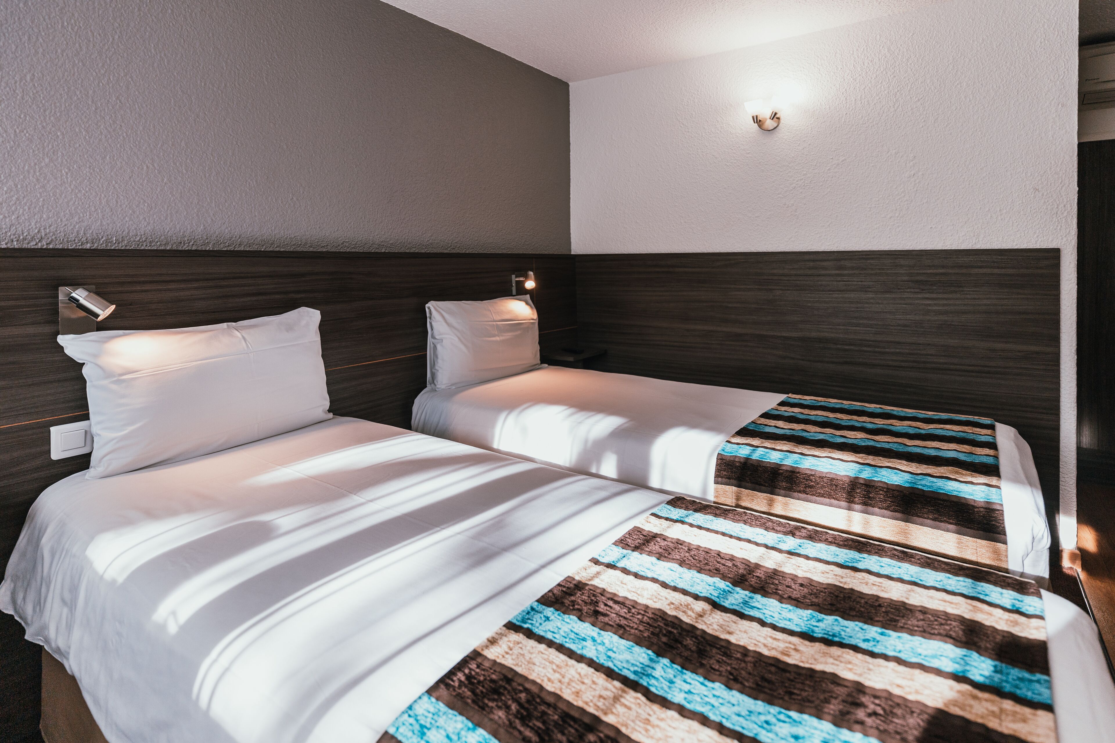 A hotel room with two beds, each with white bedding and a striped blanket.