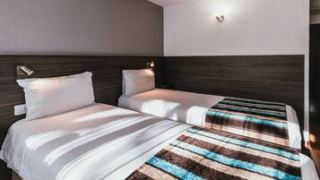 A hotel room with two beds, each with white bedding and a striped blanket.