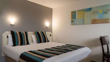 Habitación de hotel con cama, dos lámparas de pared, un cuadro y una silla.