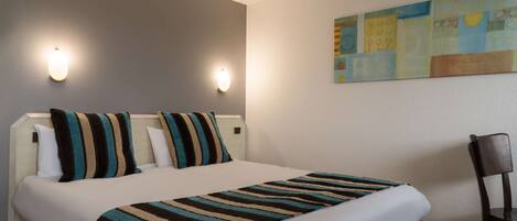 Habitación de hotel con cama, dos lámparas de pared, un cuadro y una silla.