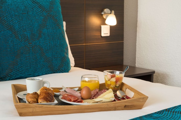 A breakfast tray with croissants, meats, cheese, a coffee cup, orange juice, and fruit on a bed in a hotel room. - Sure Hotel by Best Western Biarritz Aeroport (Biarritz)