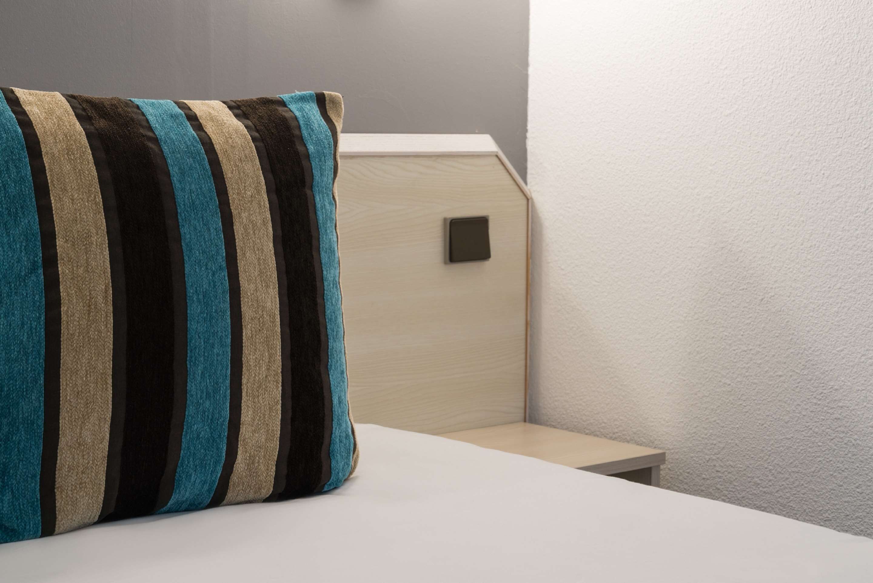 Una cama bien hecha con un almohadón a rayas y una mesita de noche.