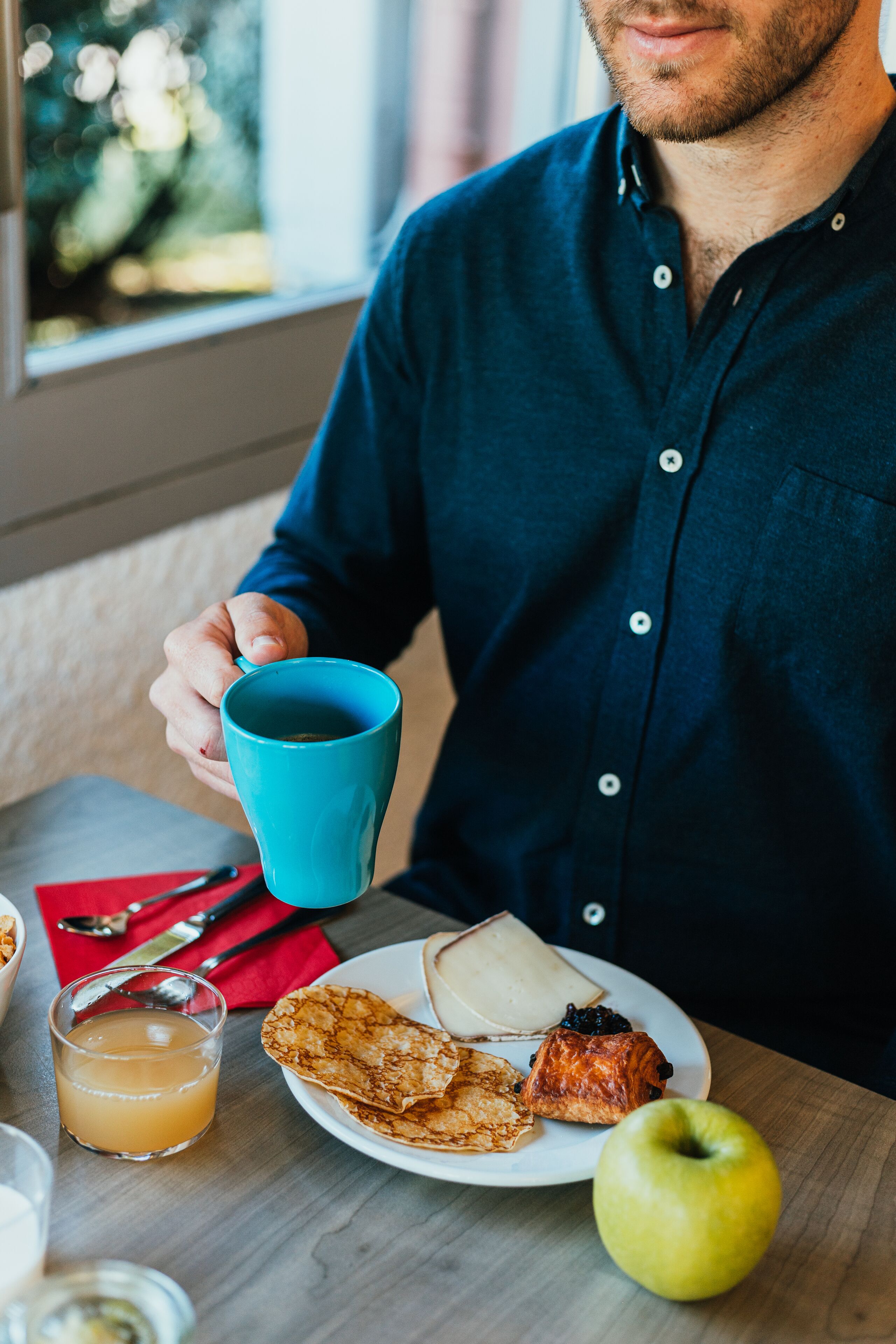 A person sitting at a table with a plate of food, a blue mug, and a glass of orange juice.
