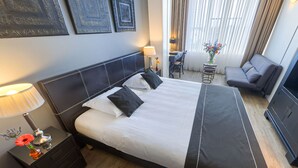 A hotel room with a large bed, a desk with a chair, a sofa, and a TV. - Hotel Chariot (Aalsmeer)