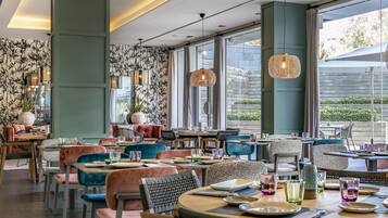 Un restaurante con mesas redondas, sillas acolchadas y lámparas colgantes de ratán.