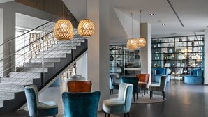 A modern lobby with a staircase, blue velvet chairs, and hanging lamps. - Hotel Vincci Maritimo (Barcelona)