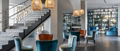 A modern lobby with a staircase, blue velvet chairs, and hanging lamps.
