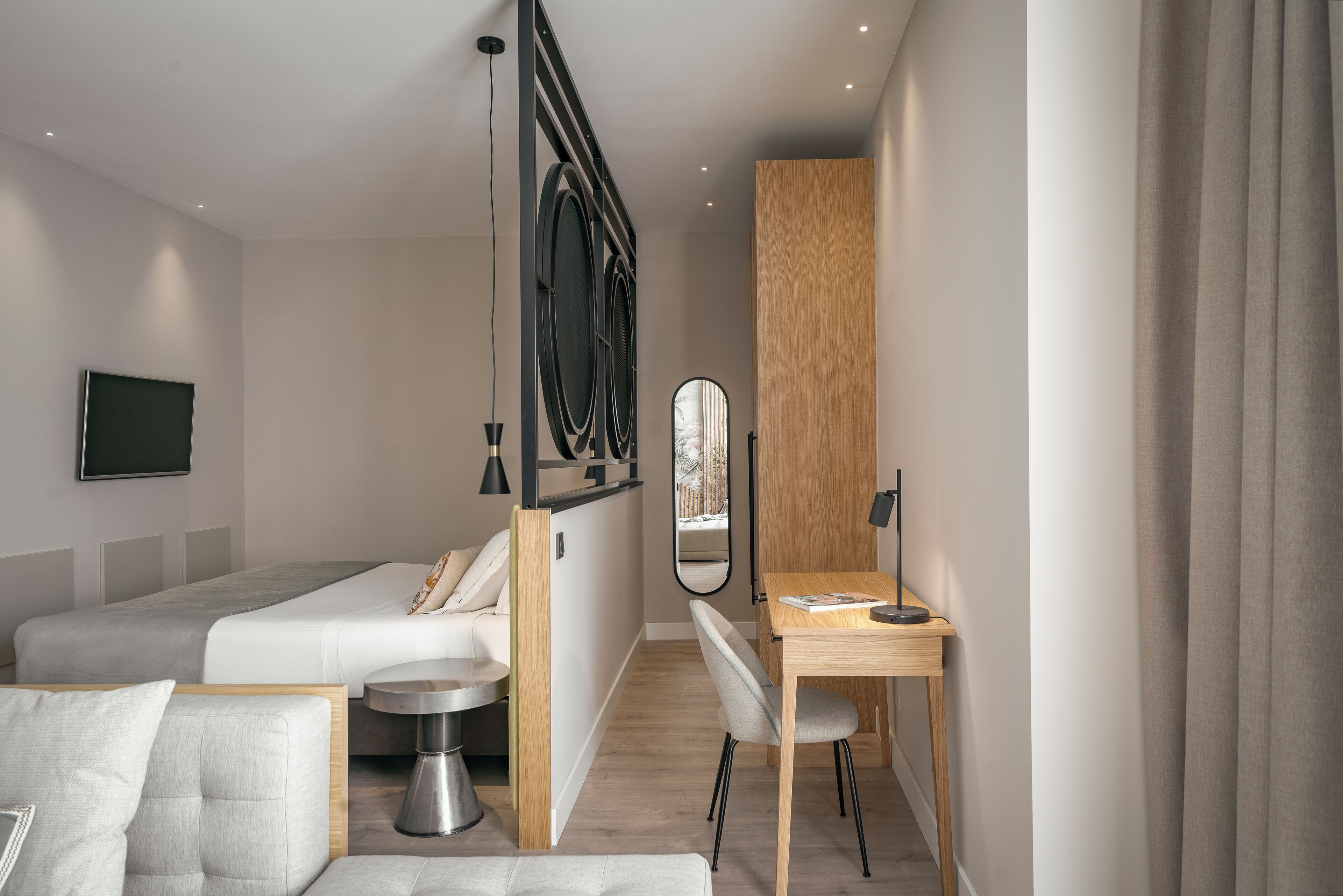 A modern hotel room with a bed, a desk, a chair, a small round table, and a mirror.