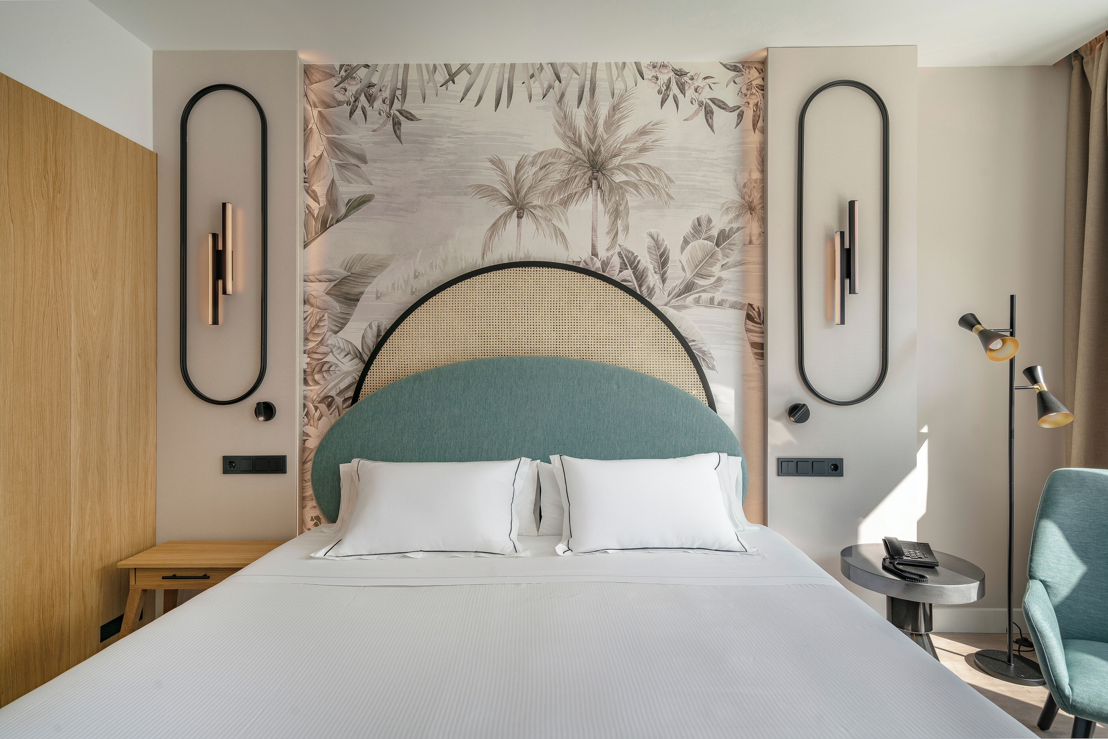 Een moderne hotelkamer met een groot bed, een hoofdbord met een groene kussen, een wandtelefoon en een klein bijzettafeltje.