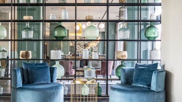 A modern interior with two blue velvet armchairs, a gold wire table, and a glass display wall with various decorative items. - Hotel Vincci Maritimo (Barcelona)