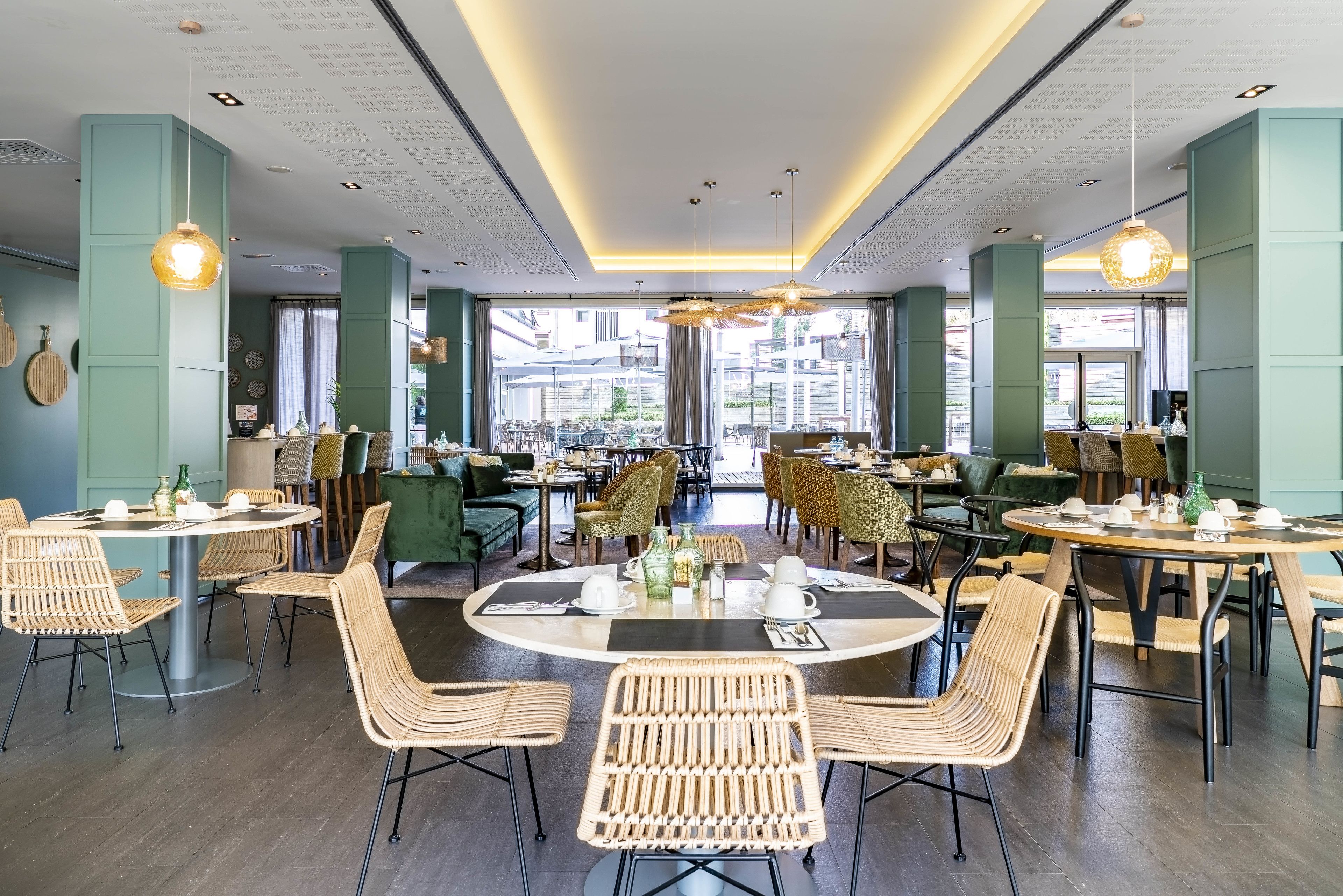A modern dining area with round tables and wicker chairs, large windows, and a ceiling with text.