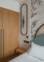 A bedroom with a wooden wardrobe, a bedside table with a drawer, a bed with white bedding, and a wall-mounted light fixture.