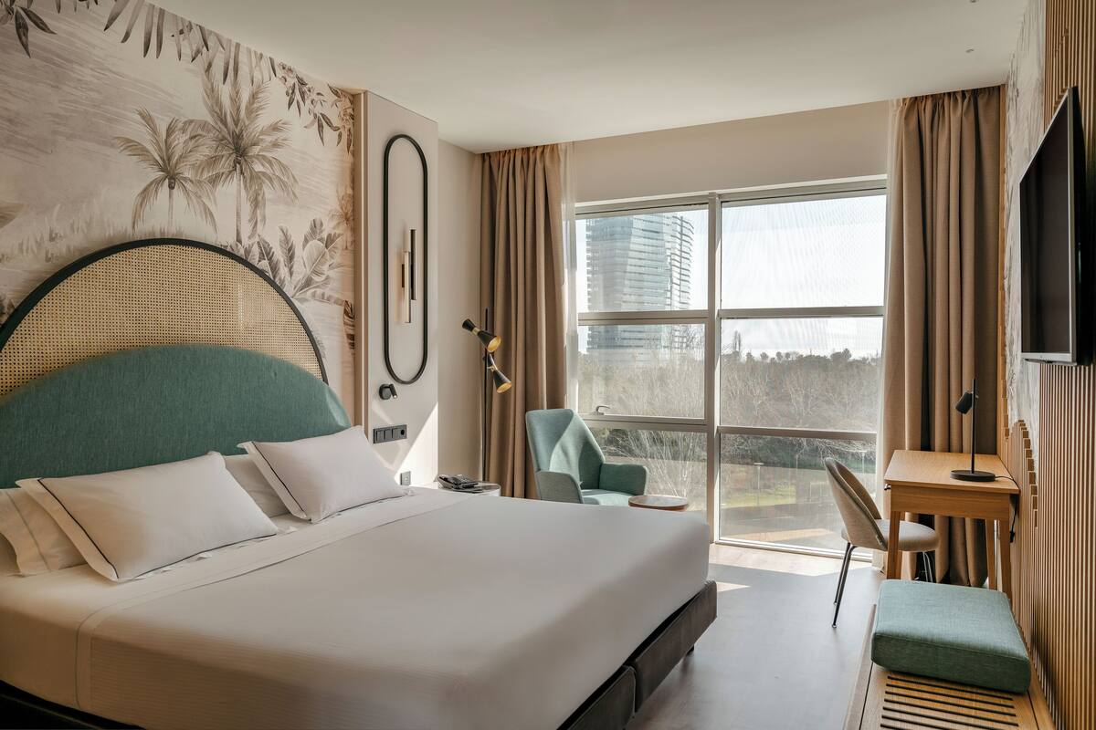 Moderni hotellihuone, jossa on suuri sänky, työpöytä, tuoli ja näkymä kaupunkiin.