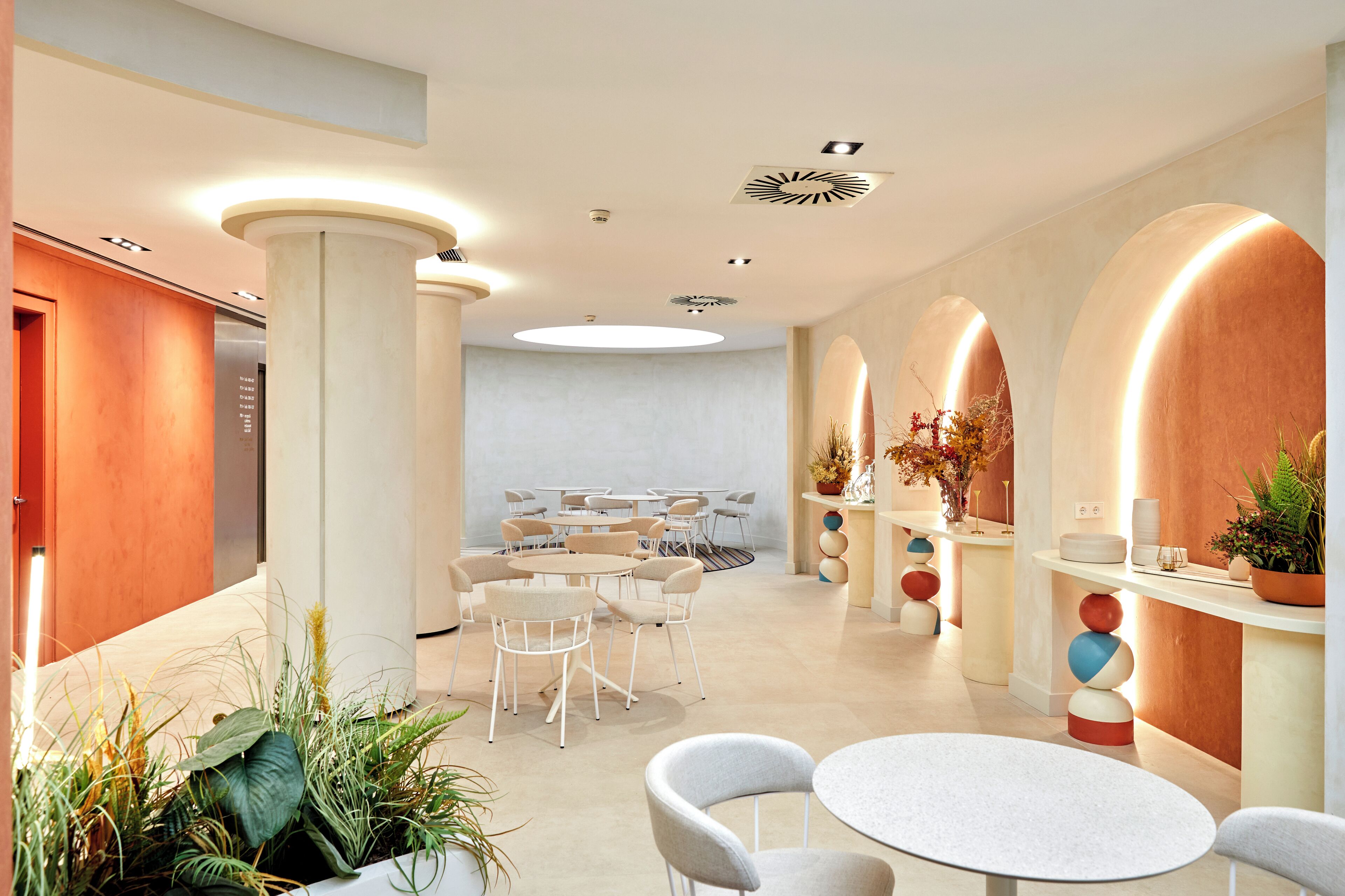 Un moderno vestíbulo de hotel con mesas redondas, sillas blancas y un área de estar central.