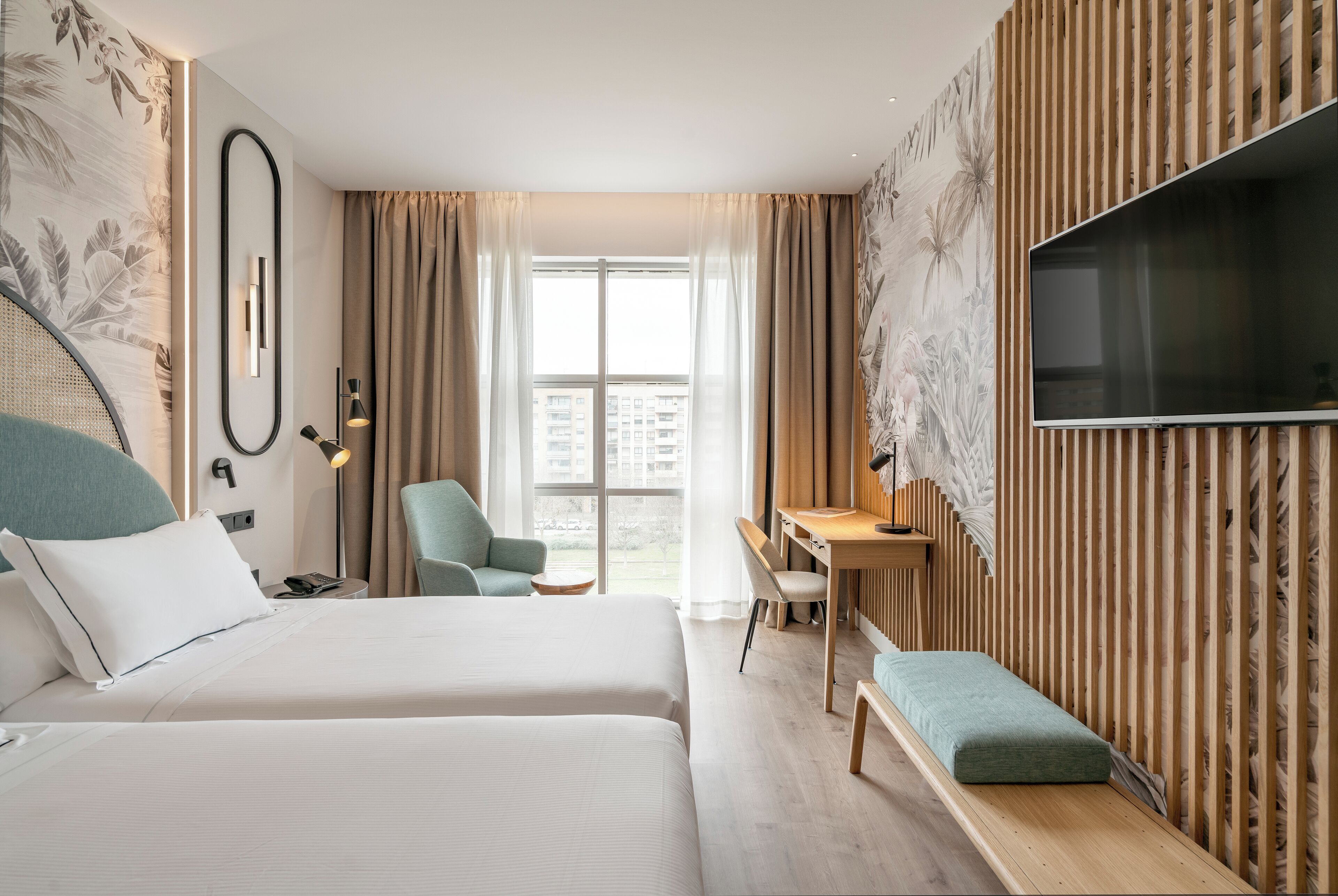 A hotel room with two beds, a desk, a chair, a TV, and a balcony with a view.