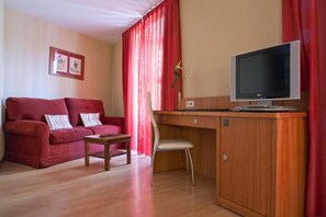 Quarto com sofá vermelho, secretária de madeira, televisão e uma cadeira.