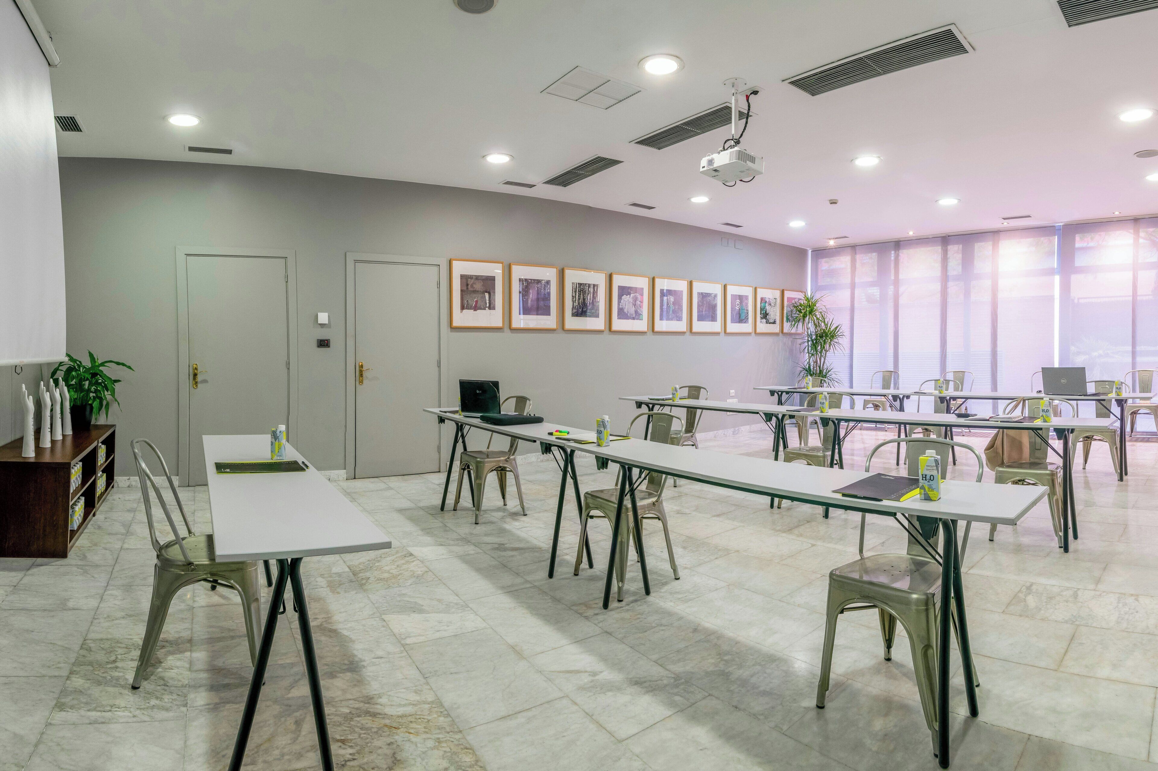 A conference room with tables and chairs, a projector, framed pictures on the wall, and a door.