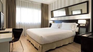 Una habitación de hotel con cama, escritorio, silla y un espejo grande.