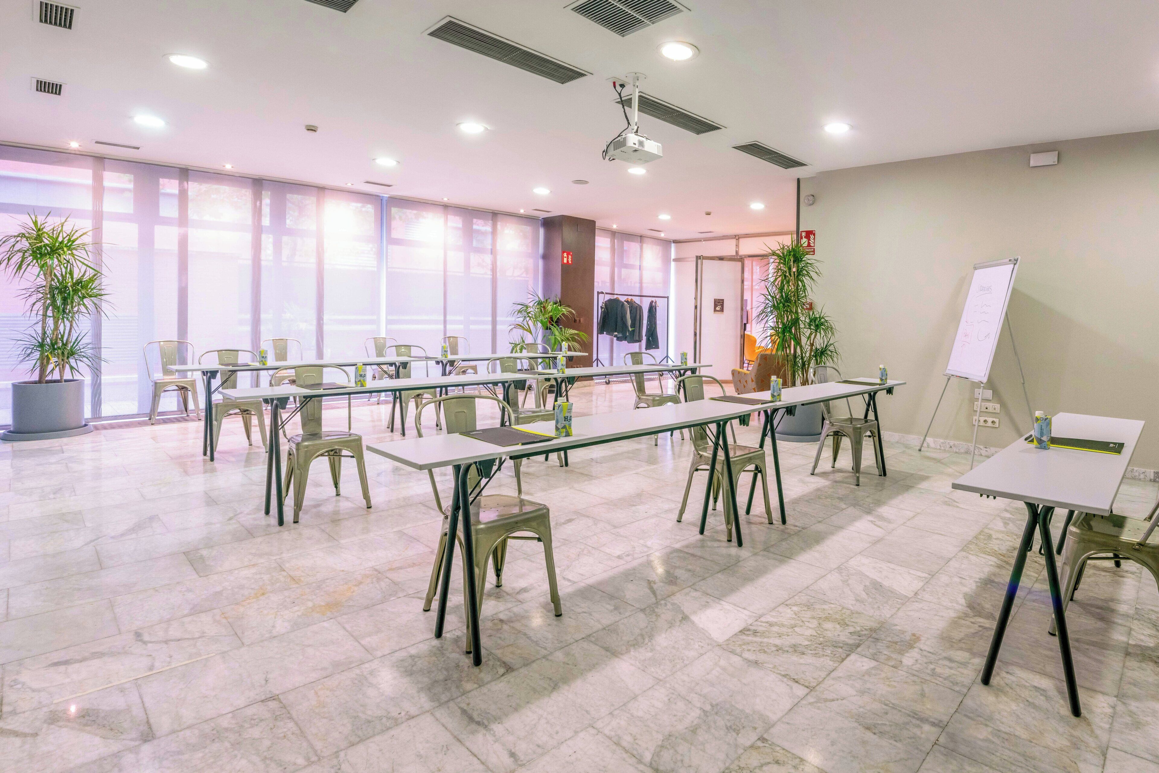 Une salle de conférence équipée de plusieurs tables et chaises, d’un tableau blanc et de plantes en pot.