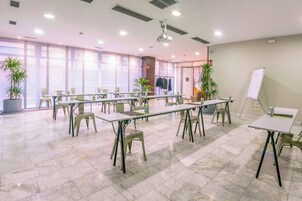 Una sala conferenze con diversi tavoli e sedie, una lavagna e piante in vaso.