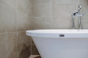 Ein modernes Badezimmer mit einer freistehenden Badewanne, chromfarbenen Armaturen und gefliesten Wänden.