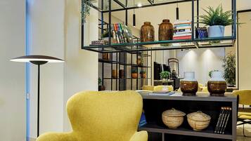 A yellow armchair, a round side table, a bookshelf with decorative items, and a floor lamp.