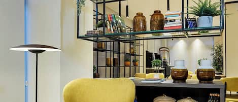 A yellow armchair, a round side table, a bookshelf with decorative items, and a floor lamp.