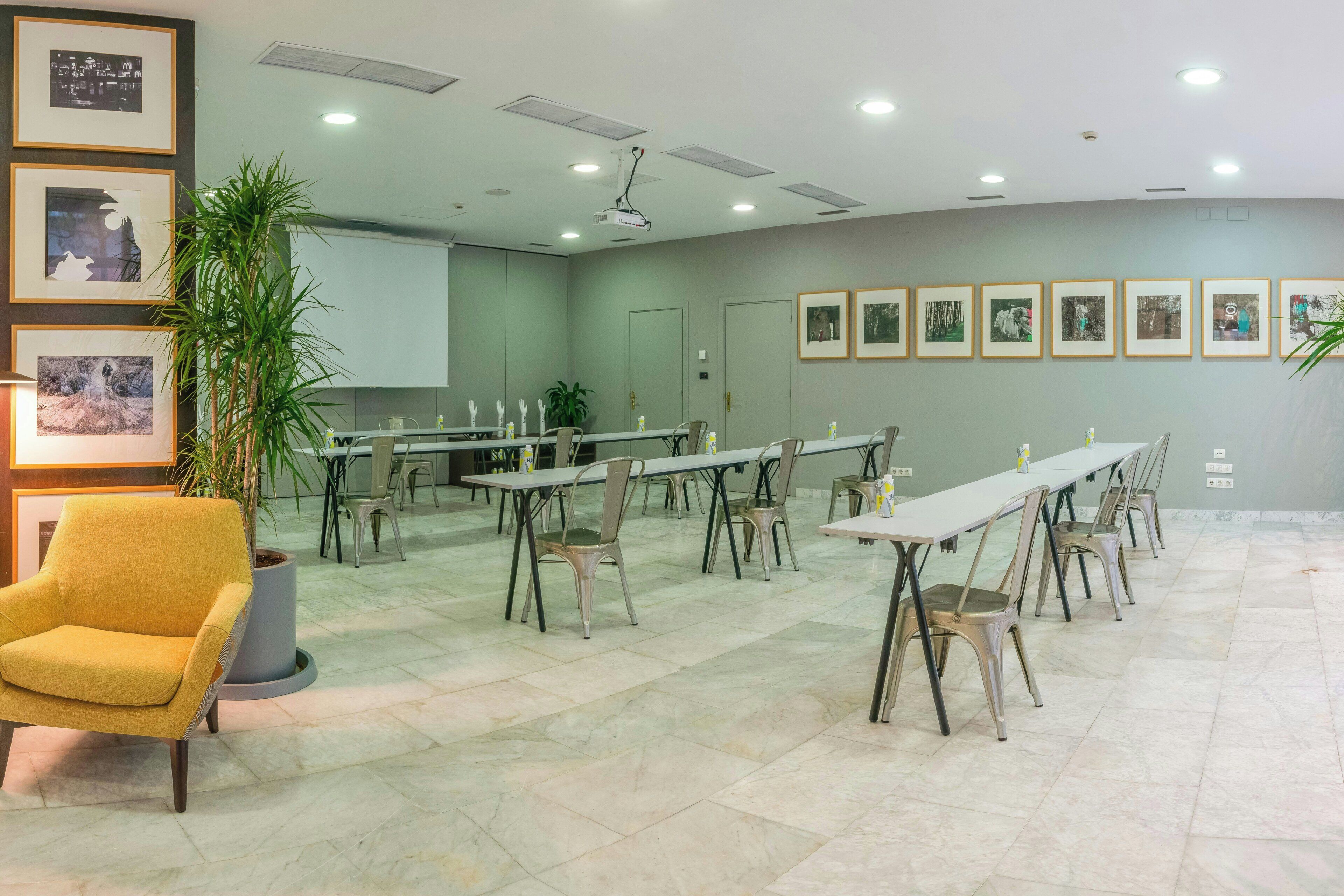 A conference room with tables and chairs, a potted plant, and framed pictures on the wall.