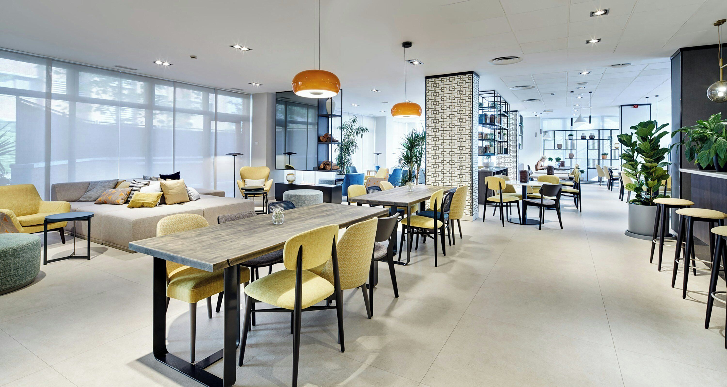 Un comedor moderno con una mesa larga, sillas amarillas y una variedad de opciones de asiento, incluyendo sofás y sillas individuales.