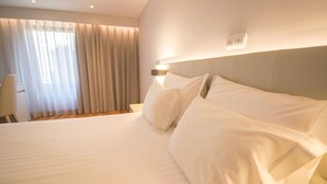 A hotel room with a large bed, a bedside table, a lamp, and a window with curtains.