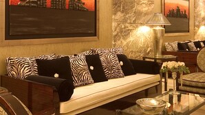 A modern living room with a sofa, chairs, a glass coffee table, and two framed artworks on the wall.